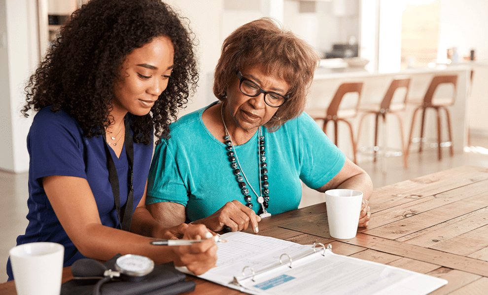 A healthcare worker reviewing medical records with an elderly woman. 